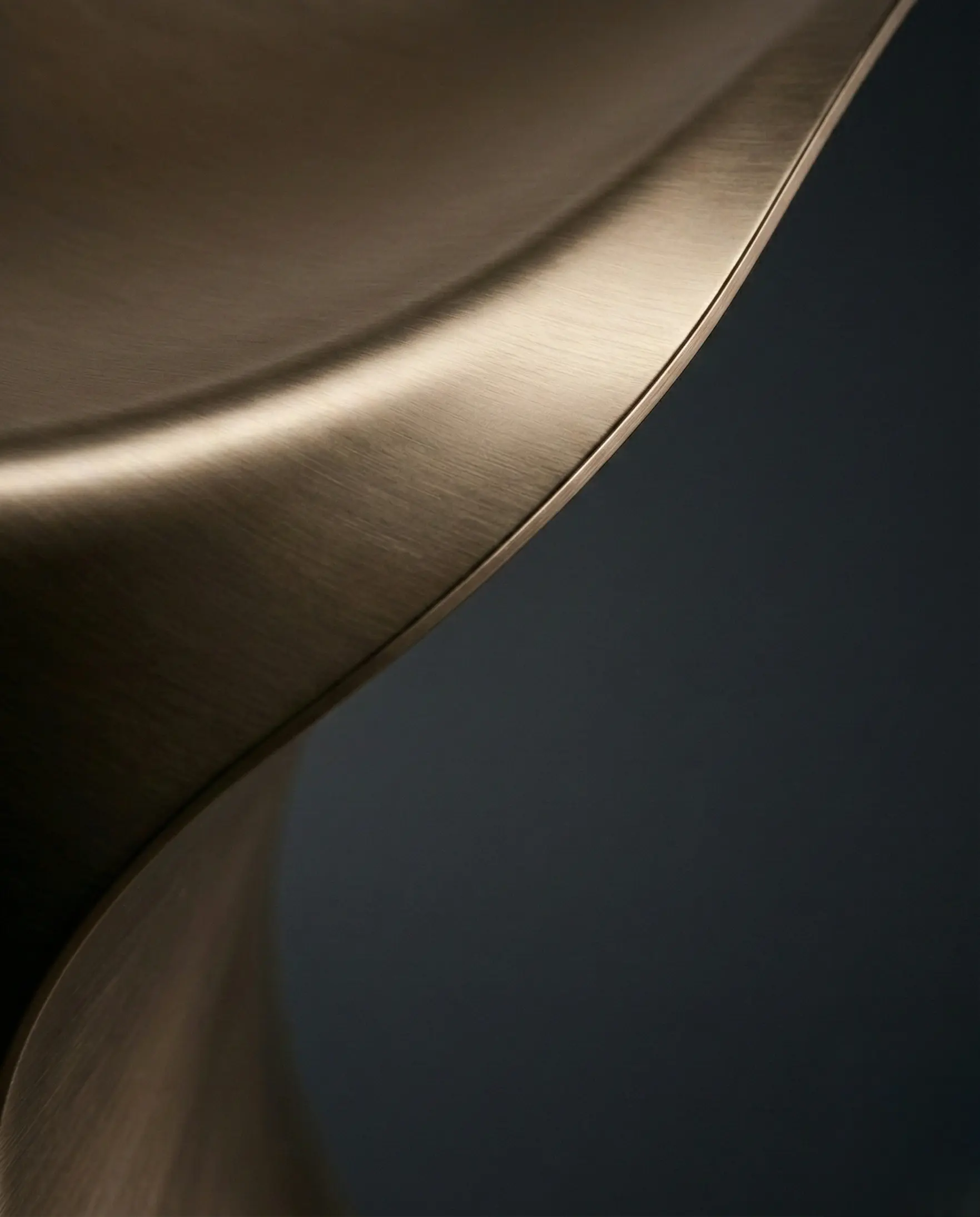 Brushed brass MetaliQ liquid metal coating detail showing a seamless curved edge and soft reflections