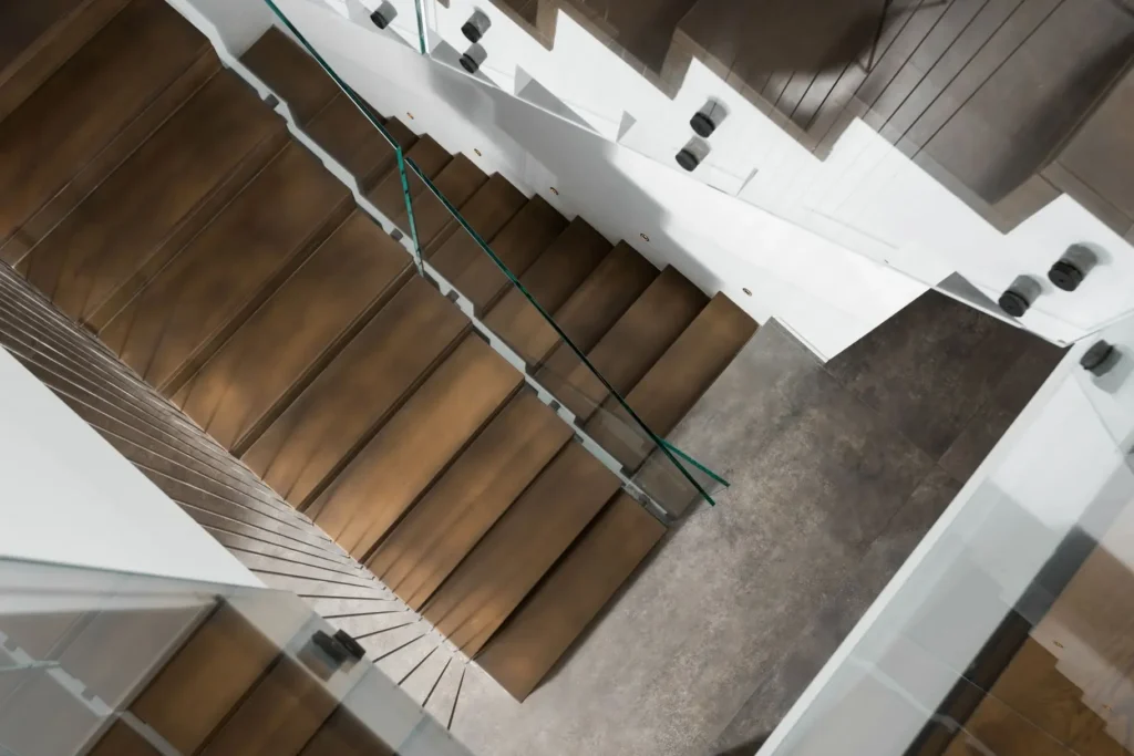 Double staircase finished in darkened brushed bronze with glass balustrade.